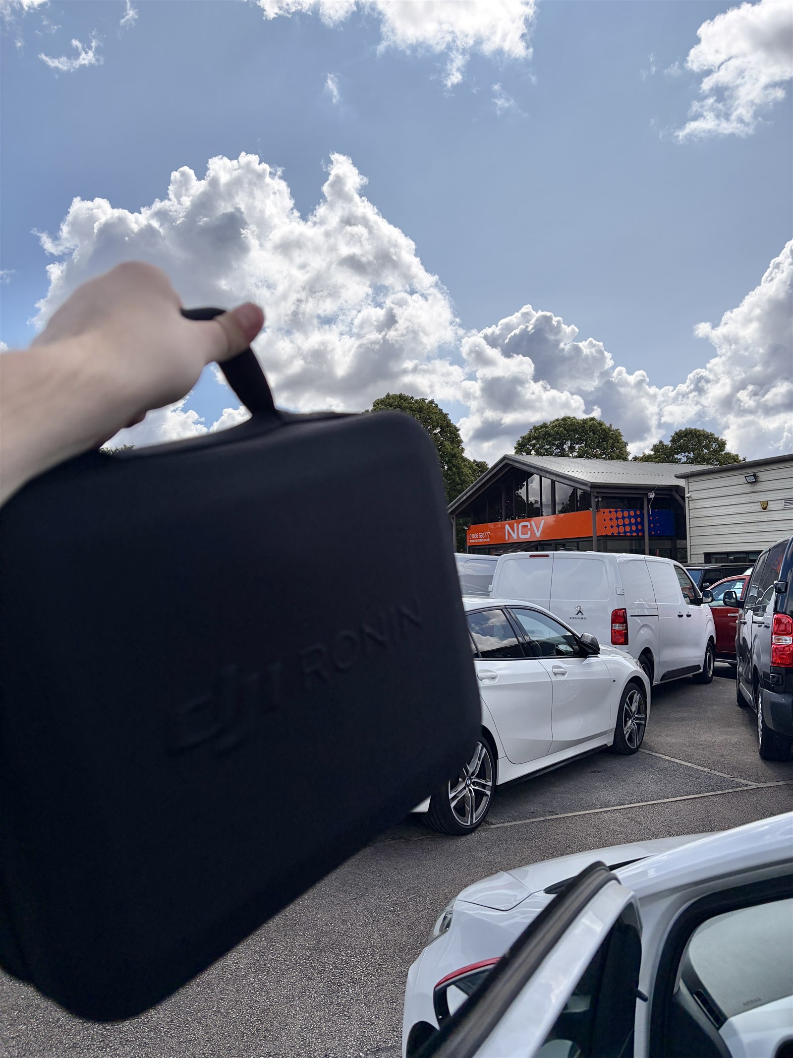 Camera equipment being carried into an NCV Sales shoot beneath a bright, cloud-filled sky